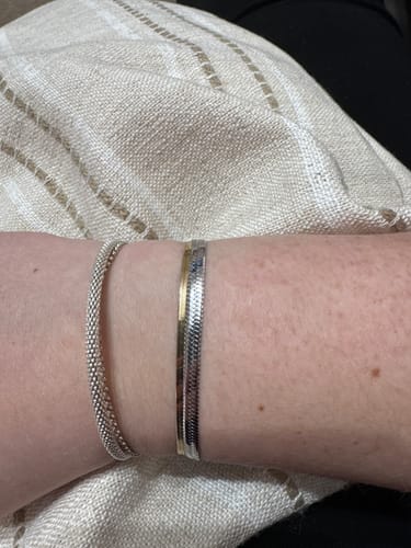 Customer wearing the shiny herringbone Essentials Bracelet stacked with a slim silver bracelet on their wrist.