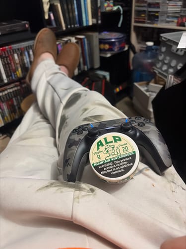 Reviewer relaxing with a tin of Mountain Wintergreen Nicotine Pouches balanced on a video game controller on their lap.