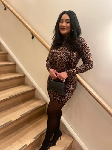 Reviewer standing on a staircase, wearing the long-sleeved, bodycon Naked Print Mini Dress.