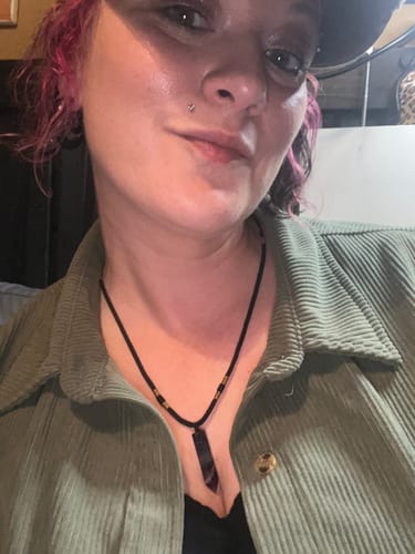 Reviewer wearing their monthly crystal necklace, which has a dark, pointed crystal on a black cord.