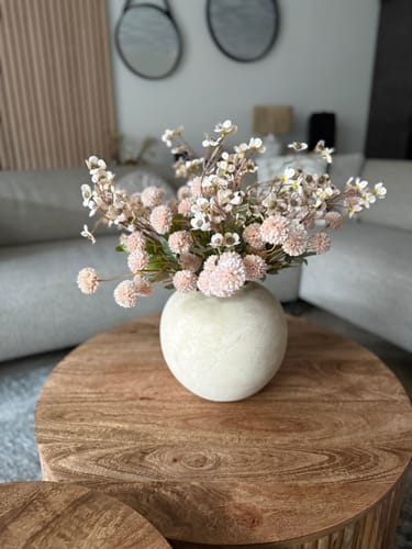 Klant toont de ronde, beige Terra vaas met een boeket bloemen op een houten salontafel.