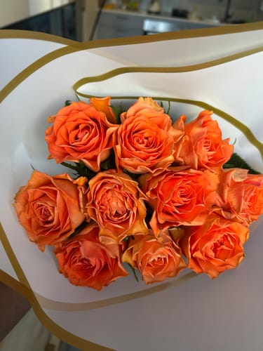 Customer's photo of the Sunset Serenade bouquet, a cluster of vibrant orange roses in paper wrapping.