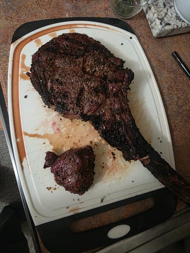 Customer's cooked Tomahawk Steak resting on a cutting board with a small piece cut off.