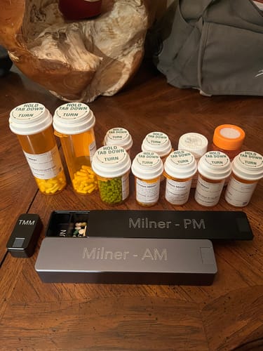 Reviewer's black Nano Case sits on a table next to larger AM/PM cases and many prescription medication bottles.