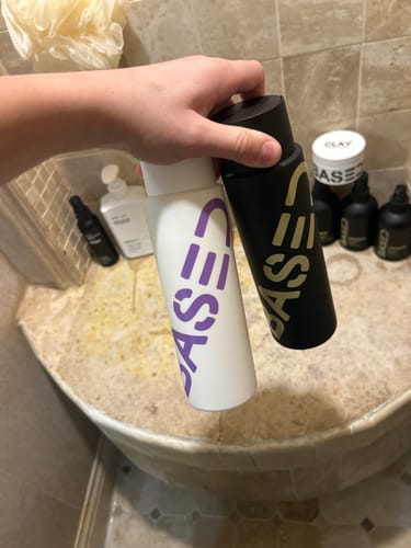 Reviewer holding the black and white Shower Duo shampoo and conditioner bottles in a bathroom.