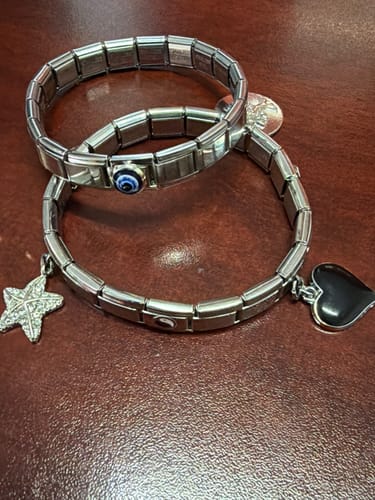 Reseña de cliente: dos pulseras italianas para charms sobre una mesa, decoradas con dijes de estrella, corazón y ojo turco.