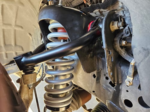Close-up of a customer's black Upper Control Arm installed on a truck, showing its position over the coil spring.