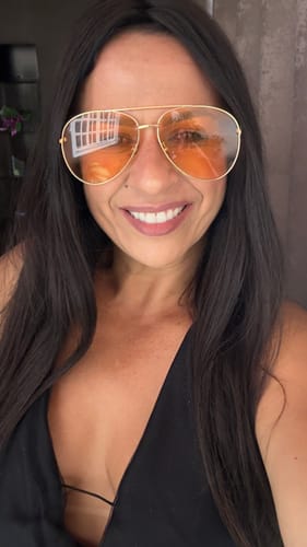 Cliente sorrindo, usando os óculos Savona com lentes laranjas e armação dourada.