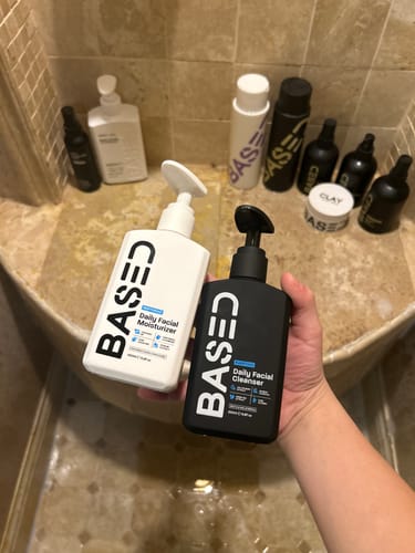 Reviewer holding the Daily Skincare Duo, a black cleanser and white moisturizer, in their bathroom.