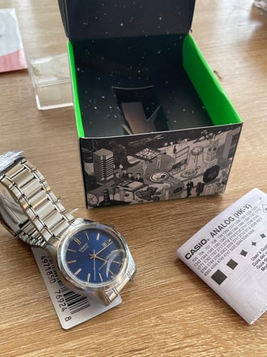 Cliente mostrando su Reloj Casio Análogo con esfera azul sobre una mesa junto a su caja.