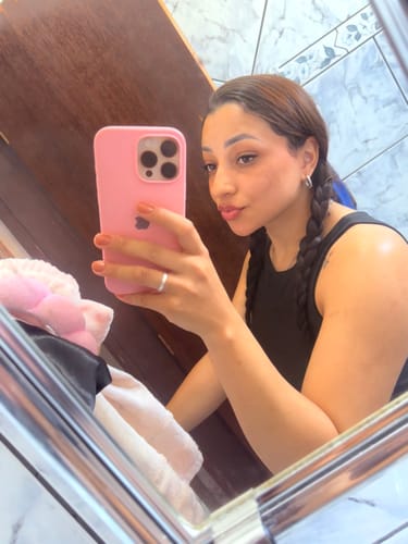 Avaliadora com cabelo escuro e trançado tirando uma selfie no espelho do banheiro.