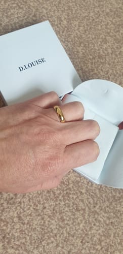 Customer's hand wearing the sleek gold Classic Stacking Ring in front of its open packaging.