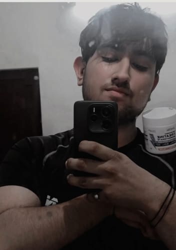 Reviewer taking a mirror selfie while holding a white tub of Wellcore Pure Micronised Creatine Monohydrate.