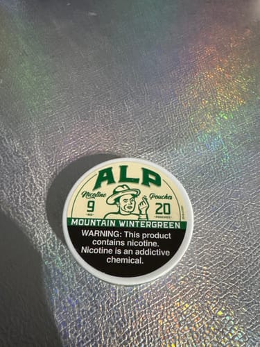 Customer's can of ALP Mountain Wintergreen Nicotine Pouches on a shiny, textured surface.