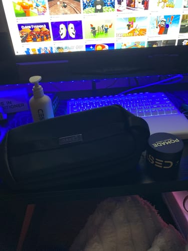 Customer's black toiletry bag on a desk next to a backlit keyboard and hair products.