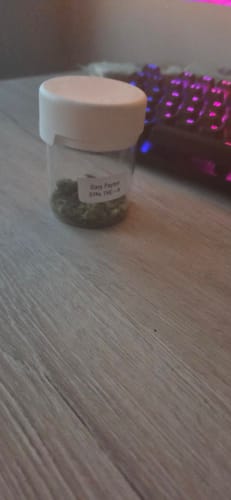 Customer's clear jar of Gary Payton 31% THCA flower on a wooden desk with a keyboard in the background.