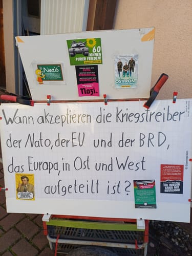 Rezensent zeigt den Aufkleber auf einem selbstgebauten Info-Wagen neben anderen politischen Botschaften und Stickern.