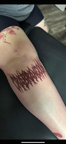 Customer's new red tattoo on their shin, completed on a painful spot with help from the numbing cream.