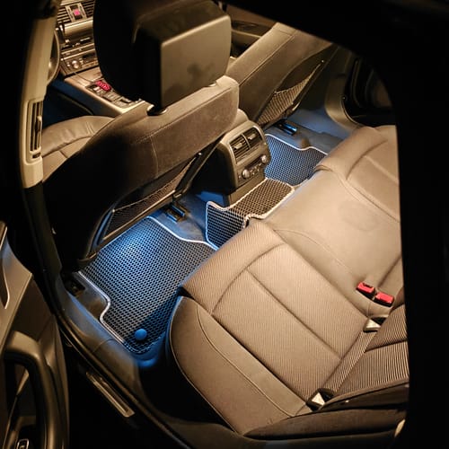 Klient pokazuje tylne dywaniki samochodowe w oświetlonym wnętrzu samochodu w nocy.