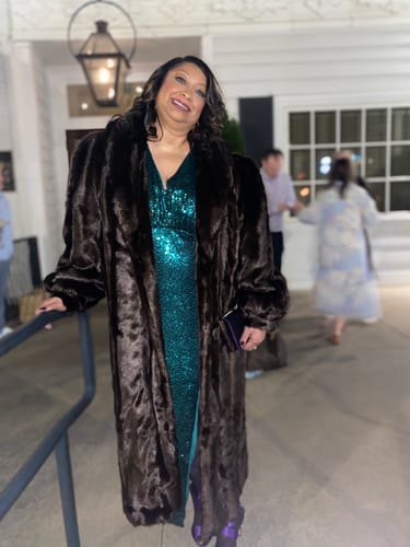 Reviewer smiling at night, wearing the plush Faux Mink Long Coat open over a sparkly green dress.
