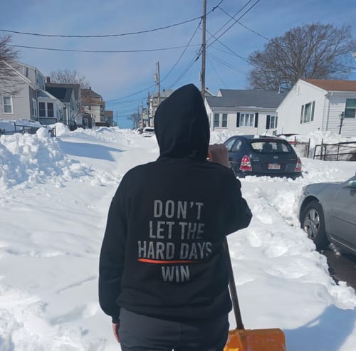 Reviewer from behind in a black Hard Days - Hoodie, standing on a very snowy street with a shovel.