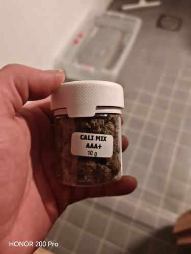 Customer holding a small, clear 10g jar filled with CALI MIX AAA+ buds against a tiled background.