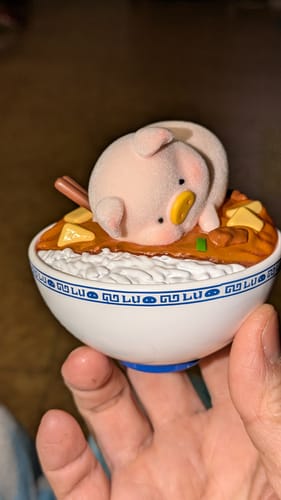 Customer holding a flocked pink LuLu the Piggy figure resting in a white and blue bowl of food.