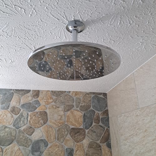 Customer's newly installed 12 Inch Rain Shower Head mounted to a ceiling in a shower with stone walls.