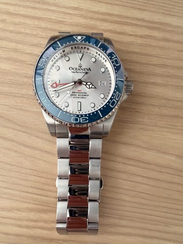 Customer's stainless steel bracelet with polished center links attached to a watch with a silver dial and blue bezel.
