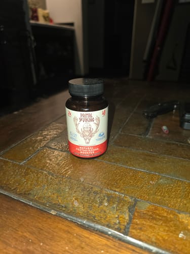 Reviewer's bottle of Primal Reindeer Testosterone Support sitting on a dark wooden table.