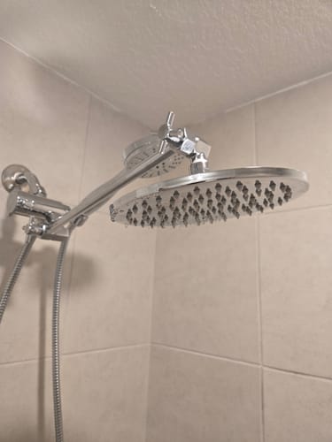 Reviewer's installed chrome Dual Shower Head with an adjustable arm in a tiled shower.