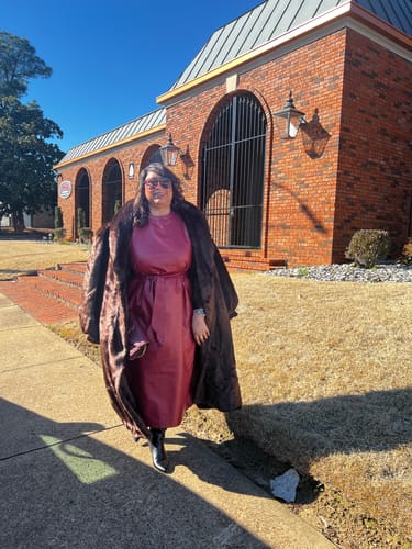 Reviewer stands outside on a sunny day wearing the oversized Faux Mink Long Coat open over a dress.