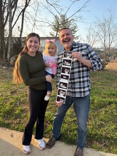 Customer's child wears the Big Sister top for an announcement, posing with family and ultrasound photos.