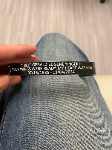 Customer's hand holding a black memorial bracelet with custom white text engraved on it.