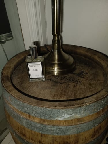 Customer's 472 Inspired by Seychelles perfume bottle sitting on a rustic wooden barrel table next to a lamp.
