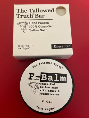 Reviewer's round black container of F-Balm, placed in front of a box of The Tallowed Truth Bar soap.