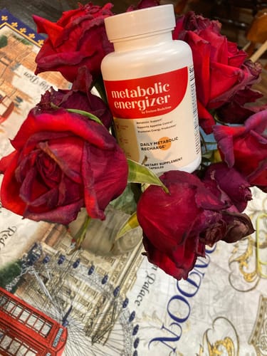 Customer's bottle of Metabolic Energizer nestled amongst several red roses on a decorative cloth.