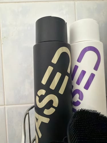 Customer's matte black shampoo bottle sitting in a shower caddy next to a scalp brush.