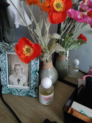 Customer's Spiced Vanilla fragrance bottle on a dresser next to a framed photo and a vase of flowers.