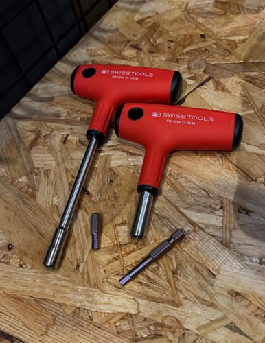Customer's two red PB Swiss Tools cross-handle bit holders in different sizes with bits on a workbench.