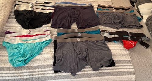 Customer's collection of various underwear styles, including the red Nylon Mesh Thong, laid out on a bed.