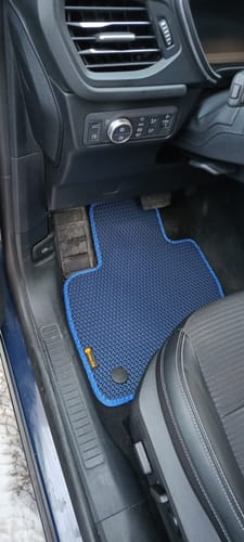 Recenzent pokazuje niestandardowy niebieski dywanik samochodowy zainstalowany po stronie kierowcy.