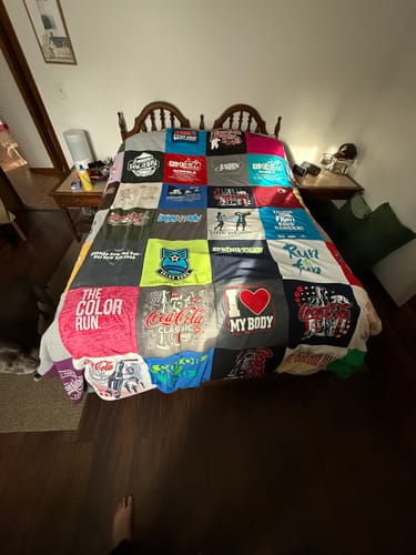 Customer's large, colorful Premium T Shirt Quilt made from various memory shirts, spread across a bed in a bedroom.