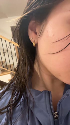 Close-up of a reviewer's ear wearing the gold Mini Drop Huggies earring with wet hair.