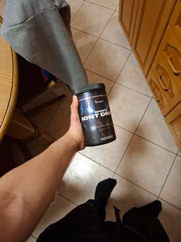 Reviewer holding a black container of Sports Iont Drink in their home.