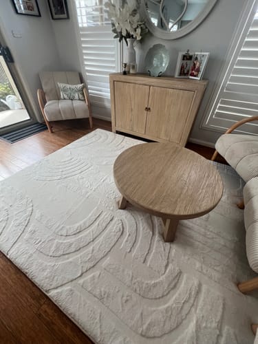 Customer's cream Cloud Haven Mellow Mat with a 3D pattern in a living room under a small wooden coffee table.