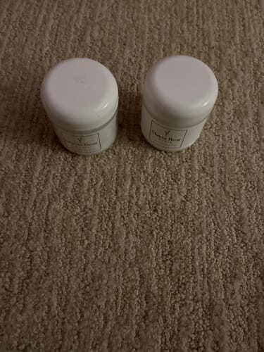 Customer's two white jars of Mama Bear Nerve Relief Lotion sitting side-by-side on a textured brown carpet.
