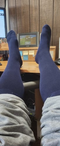 Customer wearing the dark blue compression socks with their feet resting on a desk, showing the full length.