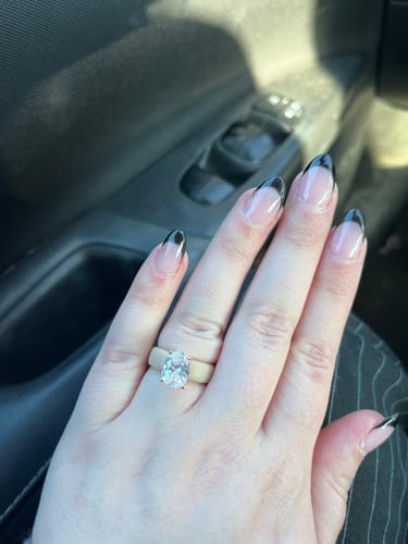 A customer's hand wearing the silicone ring with a large, oval-cut stone, shown inside a car.