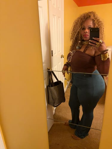 Reviewer takes a mirror selfie showing off the long, curly Bobbi Boss MIRABEL wig.